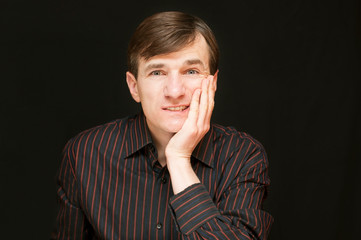 A middle-aged man holds his cheek and suffers because he has a toothache