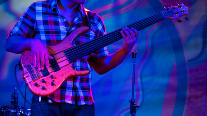 Obraz na płótnie Canvas Close up shot - male bassist hands playing bass guitar on stage of ethnic open air concert. Entertainment, music, culture, leisure and art concept