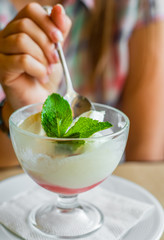 young girl's hand holding a spoon and  eating ice cream in glass at a table in cafe