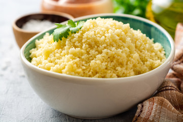 Cooked couscous with cilantro in ceramic bowl on concrete background. Selective focus.
