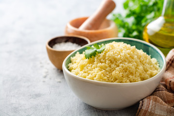 Cooked couscous with cilantro in ceramic bowl on concrete background. Selective focus.