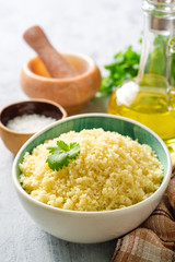 Cooked couscous with cilantro in ceramic bowl on concrete background. Selective focus.