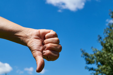 Thumbs down in front of a blue sky; negativ 
