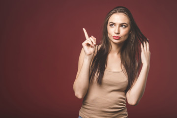 Photo of happy young woman standing isolated over red wall background. Showing copyspace pointing.