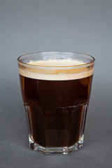 large transparent glass filled with cold summer drink of American coffee or a coffee filter photographed on a gray isolated background, photo for the menu