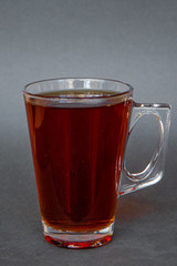 a transparent mug with a handle filled with hot bright tea of intense color on a dark gray background, the photo is suitable for the menu of cold tea in the cafe