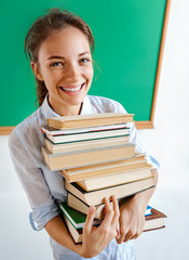 Young girl holds stack of books near blackboard, education concept. Back to school!!