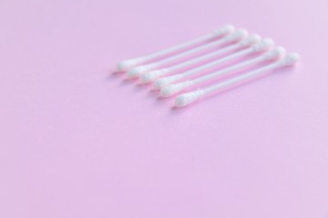 Row of white clean cotton swabs with selective focus on pink neutral background with empty space for text. Personal hygienic cotton buds for daily routine. Soft cotton ear sticks. Healthcare tools 