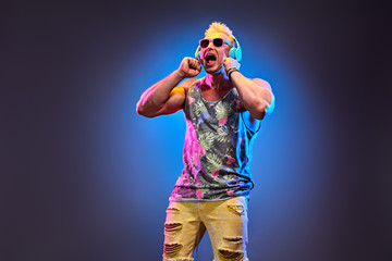 Fashion Excited Muscular DJ man dance music, colorful neon light. Handsome pumped-up blonde...