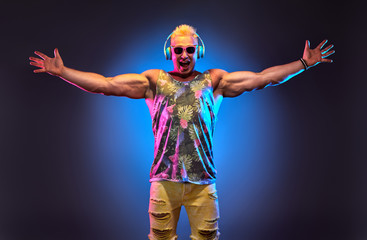 Fototapeta na wymiar Fashion Muscular DJ man listen to music in colorful neon light with hands up. Handsome blonde Hipster guy Having Fun happy. Art neon fashionable style. Music festival nightclub, summer party concept