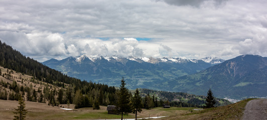 Naklejka na ściany i meble Panorama of an alpine landscape with high mountains, green meadows and trees in spring with snow in Austrian Alps