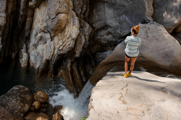 Girl with ponytail watching at waterfall in canyon