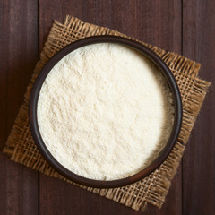 Powdered or dried milk in bowl, photographed overhead on dark wood with natural light (Selective Focus, Focus on the top of the milk powder)
