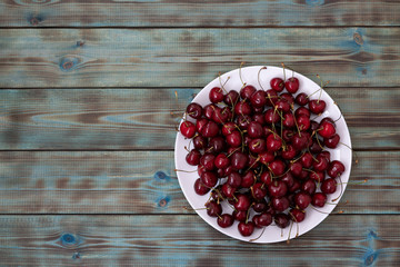 Red sweet cherry shot in a white plate on a blue wooden background close-up.
