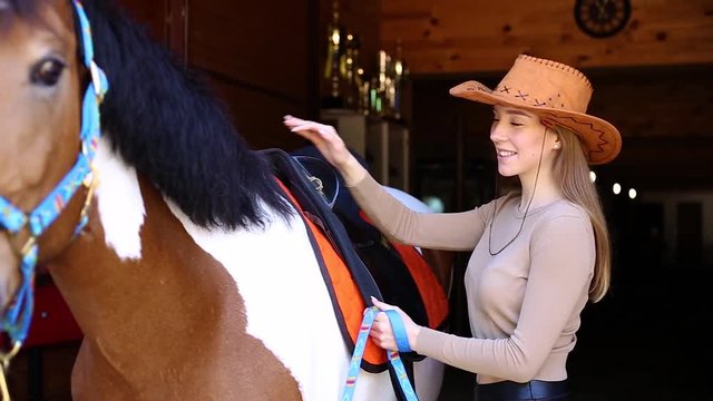 The girl wears a saddle on a horse in a cowboy hat