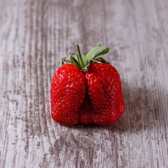 Ugly strawberry on wooden background. Trendy ugly food.