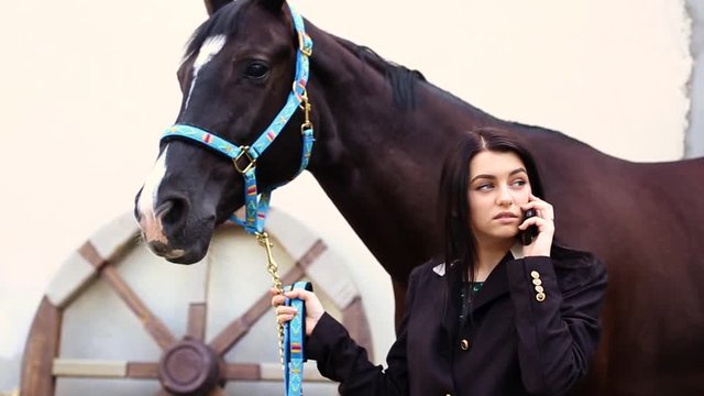young beautiful girl talking on the phone near horse