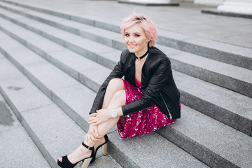 Street urban portrait of young hipster caucasian stylish sexy cheerful gorgeous woman in black suit and pink dress smiling. Happiness, fashion, beauty, freedom concept. Grey color background