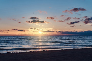 Beautiful colourful sunset at seaside with some clouds and gold reflection on water.