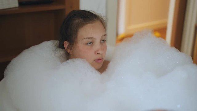 Teenager girl takes a bath full of foam.