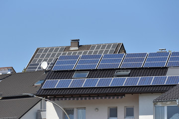 Fototapeta premium Several roofs of houses with solar panels under the blue sky. Solar panels on roofs with tiles