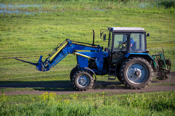 A tractor is driving along a road in a meadow. Summer sunny day. Russian province.