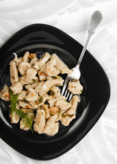 Lazy dumplings watered with green sauce with a fork on a dark plate on a textured light background.  In the Chechen, Ingush and Balkar they are called Zhur-healthmash.