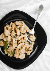 Lazy dumplings watered with green sauce with a fork on a dark plate on a textured light background.