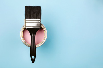 Brush with black handle on open can of pink paint on blue pastel background. Renovation concept....