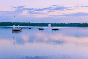 Peaceful landscape with sailboats moored on the lake  under rhe blue cloudy sky at sunset. Reflection of boats and clouds in water.