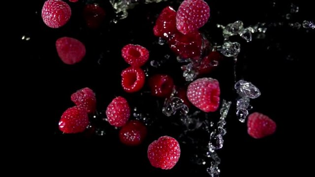 Ripe juicy raspberries with water bouncing against to the camera on a black background in slow motion super close-up