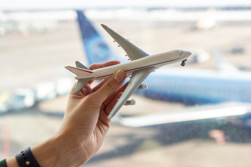 A girl holds a toy plane on the background of the airport. Concept on the theme of travel and freedom.
