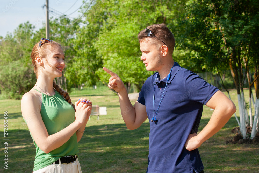 Wall mural young couple arguing while sitting on bench in park. problems in relationship