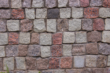 Pieces of cobblestones bricks cubes of granite red gray pink black, background texture. Granite masonry wall of an old building