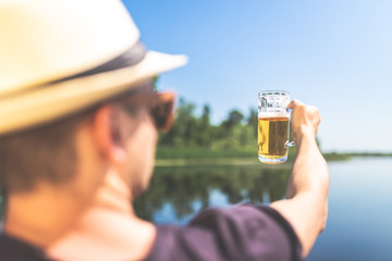 Close up of young fashionable man holding glass of beer outdoors. Summer and travel concepts.