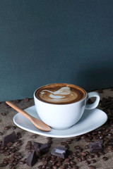 A cup of fresh coffee with a swan formed cream and a wooden spoon on the gunny sack table with coffee beans and chocolate