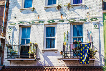 Fototapeta na wymiar A Traditional Blue and Yellow Fleur de Lis Flag hangs from a Balcony on a White Brick Building in the French Quarter of New Orleans, Louisiana, USAA Traditional Blue and Yellow Fleur de Lis Flag hangs