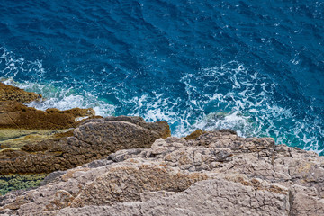 A view of the surf and rocky shore from a bird eye view on a sunny day.