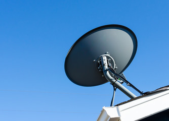 Satellite dish mounted to residential rooftop. with blue sky backdrop.