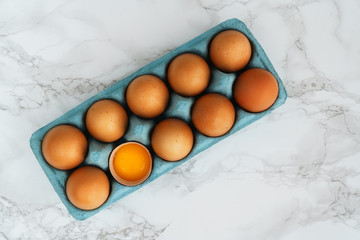 Close-up view of raw organic chicken eggs in a blue carton box. Marble table, high resolution