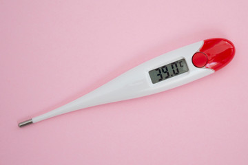 White digital clinical thermometer on pink background shows fever heat