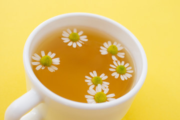 A white cup with chamomile tea on yellow background, top view