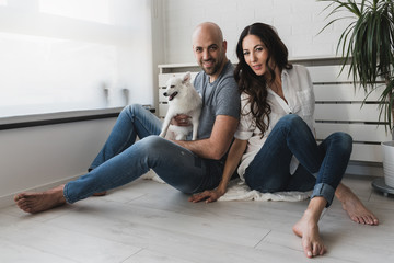 Smiling love couple expecting baby enjoying in their empty apartment with their cute white dog. How to Introduce Dogs and Babies