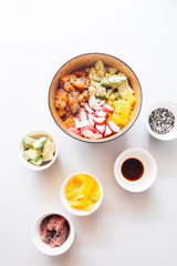 Hawaian trendy food of 2019 poke bowl, with radish tuna, salmon, jasmine rice, avocado, top view over a concrete gray backdrop, with mall bowl with ingredients, soya sauce, sesame, japanese hawaian ty