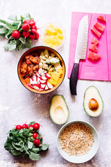Hawaian trendy food of 2019 poke bowl, with radish tuna, salmon, jasmine rice, avocado, top view over a concrete gray backdrop, with mall bowl with ingredients, soya sauce, sesame, japanese hawaian ty