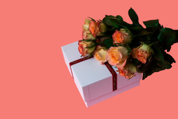 White gift box with a red ribbon on a pink background with a bouquet of pink roses. Beautiful gift...