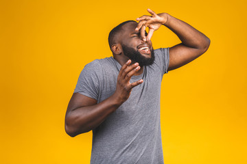 Afro american man isolated against yellow background smelling something stinky and disgusting, intolerable smell, holding breath with fingers on nose. Bad smells concept. - obrazy, fototapety, plakaty