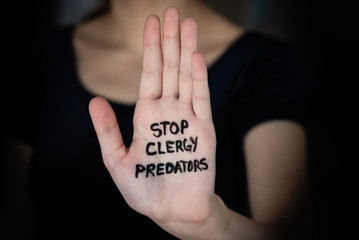Woman in darkness holding hand into light with words Stop Clergy Predators written on hand