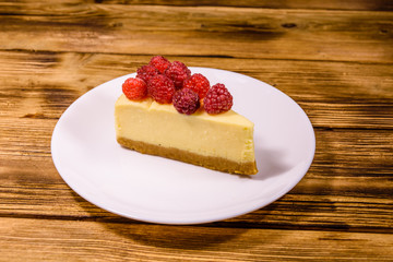 White plate with cheesecake New York and raspberries on wooden table