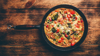 Vegetable frittata with broccoli, red bell pepper and red onion in cast iron skillet. View from...